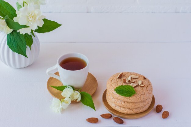 Utili biscotti quaresimali di farina di mandorle impilati su fondo di legno bianco con tazza di tè al gelsomino. messa a fuoco selettiva