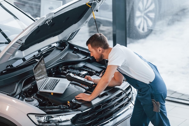 Utilizza il laptop Giovane in camicia bianca e uniforme blu ripara l'automobile