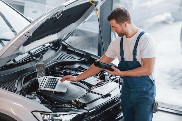 Utilizza il laptop Giovane in camicia bianca e uniforme blu ripara l'automobile