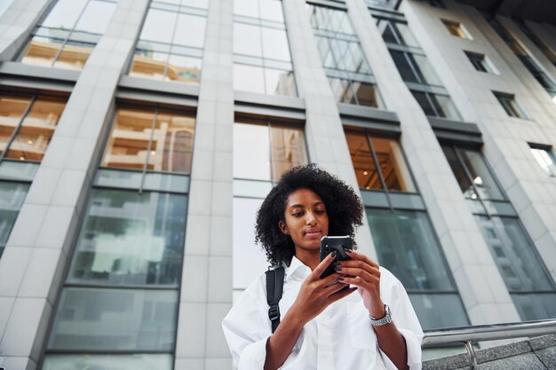 Utilizza il telefono Una donna afroamericana in bei vestiti è all'aperto in città durante il giorno