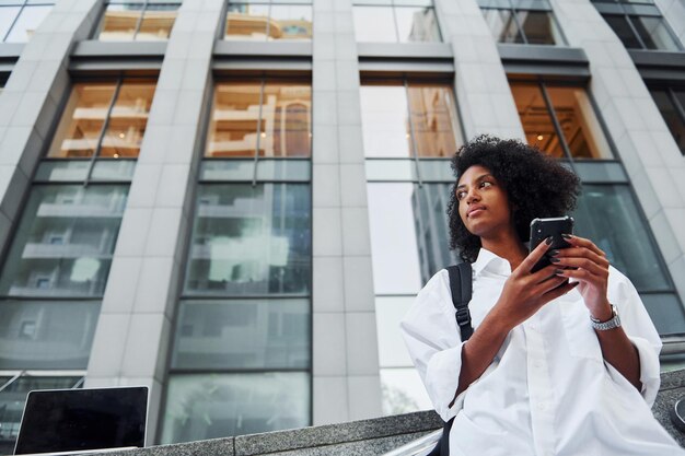 Utilizza il telefono Una donna afroamericana in bei vestiti è all'aperto in città durante il giorno