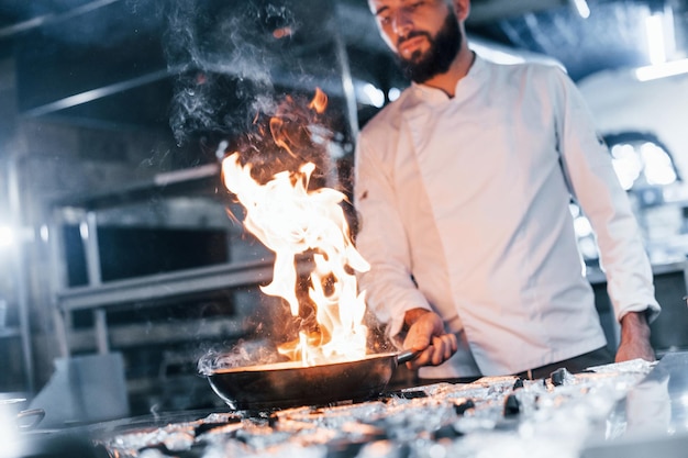 Utilizza la padella Chef in uniforme bianca che cucina il cibo in cucina Giornata intensa al lavoro