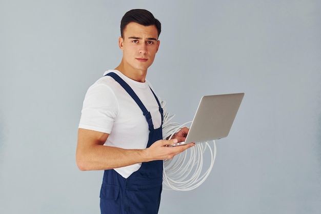 Utilizza laptop Lavoratore maschio in uniforme blu in piedi all'interno dello studio su sfondo bianco