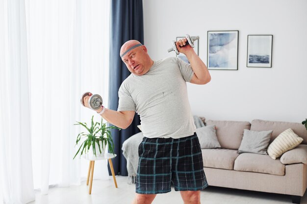 Utilizza manubri Divertente uomo sovrappeso in abiti casual è in casa a casa