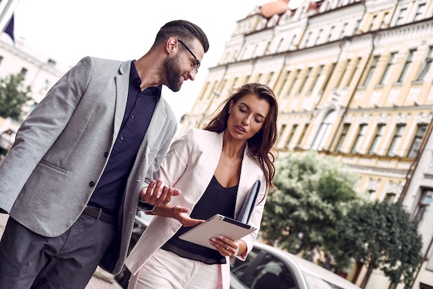 Utilizzando gadget due giovani uomini d'affari che camminano fuori sulla strada della città controllando le ultime notizie