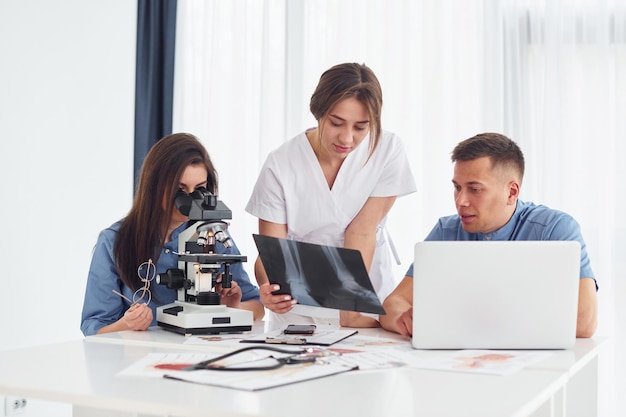 Utilizzando il microscopio Un gruppo di giovani medici sta lavorando insieme nell'ufficio moderno
