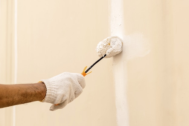 Utilizzando un rullo per dipingere di colore bianco sul muro di cemento