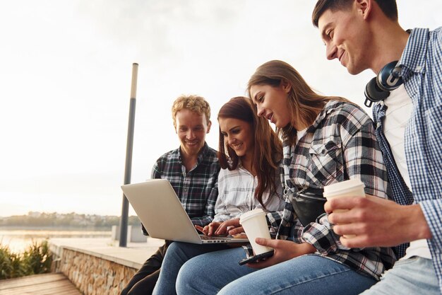 Utilizzo del laptop Gruppo di giovani amici allegri che si divertono all'aperto insieme