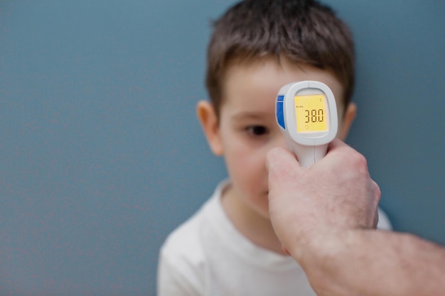 Utilizzo del termometro a infrarossi per misurare la temperatura corporea del bambino su sfondo blu