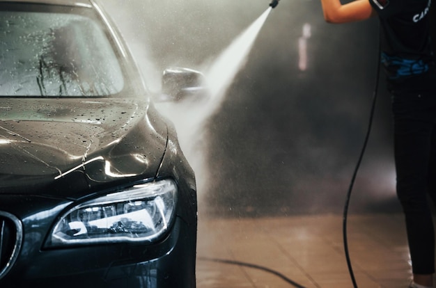 Utilizzo di apparecchiature con acqua ad alta pressione La moderna automobile nera viene pulita da una donna all'interno della stazione di lavaggio auto
