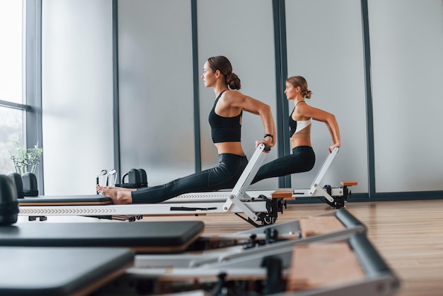 Utilizzo di attrezzature da palestra Due donne in abbigliamento sportivo e con corpi snelli hanno una giornata di yoga fitness insieme al chiuso