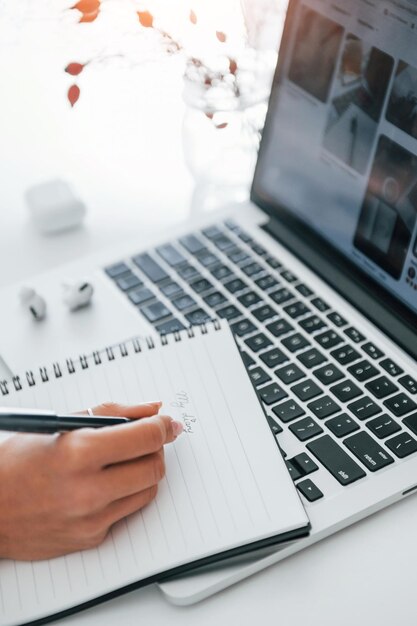 Utilizzo di laptop e blocco note Giovane freelance femminile che lavora al chiuso in ufficio durante il giorno