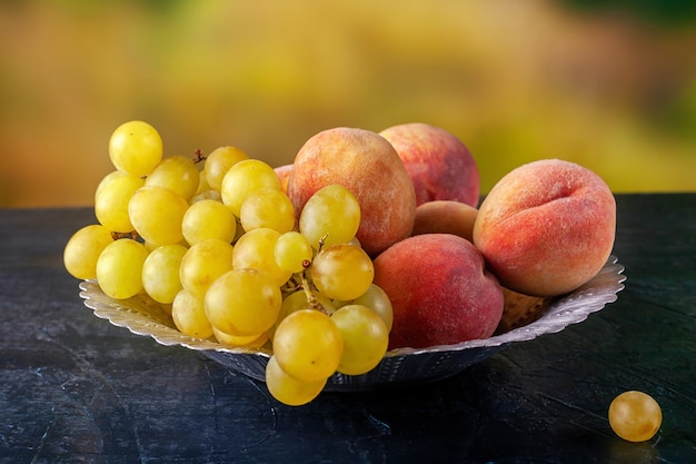 Uva e pesche mature in una ciotola di metallo all'aperto