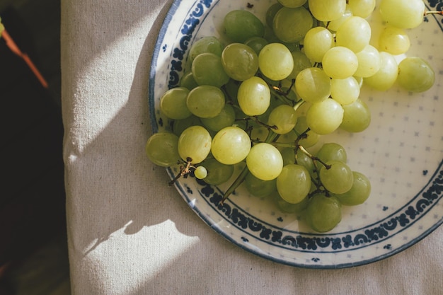 Uva fresca alla luce del sole su piatto di ceramica piatto disteso Estetica alimentare sana Frutta estiva alla luce su sfondo di lino morbido Estate in campagna bandiera lunatica