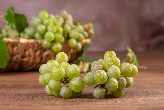 Uva, grappoli d'uva verde posti insieme a un cesto di paglia su una superficie di legno, fuoco selettivo.