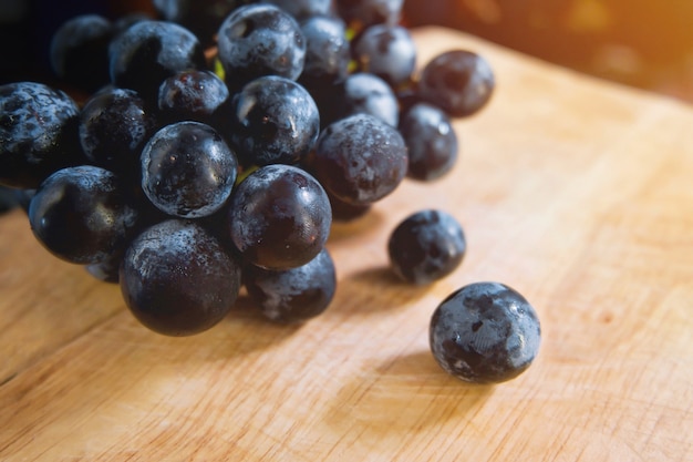 Uva nera in vassoio di legno con luce solare. Sfondo di frutta