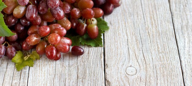 Uva rossa con foglie su un vecchio tavolo in legno da vicino