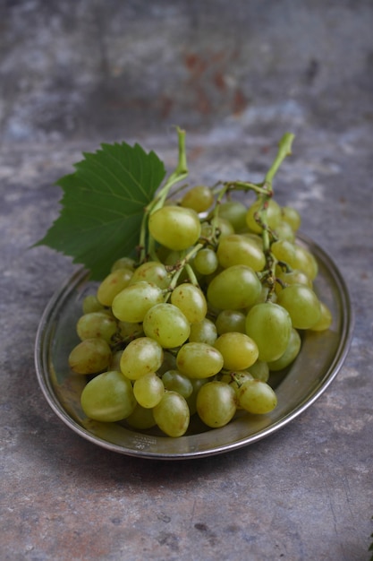 Uva verde in una placca di metallo su uno sfondo grigio