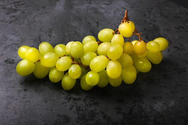 Uva verde su uno sfondo di marmo scuro. Cantina Volumetrica. Un grappolo di uva verde cespuglio.