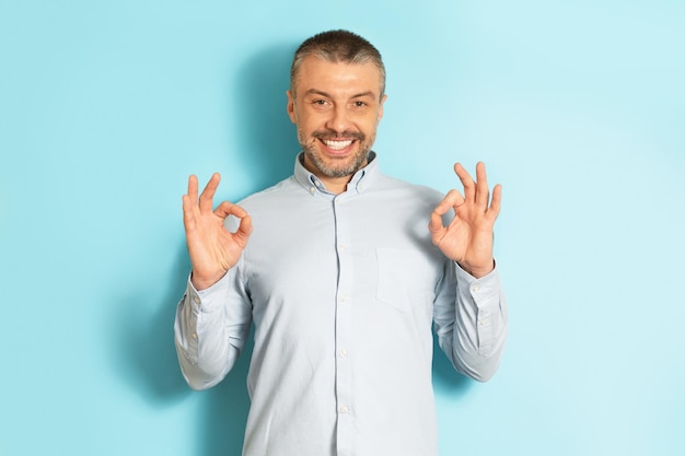 Va tutto bene Felice uomo caucasico maturo che fa il gesto di approvazione e sorride alla macchina fotografica posando su sfondo blu