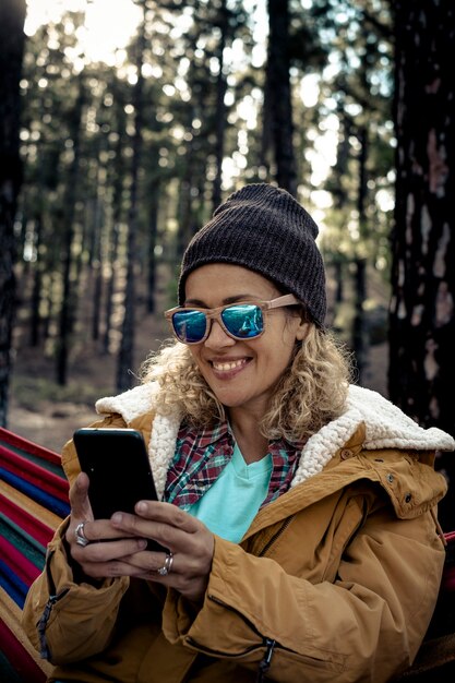 Vacanza di viaggio alternativa per le persone di sesso femminile che messaggiano con il telefono nella natura selvaggia della foresta dei boschi - bella giovane donna adulta usa la tecnologia cellulare in roaming per chattare e videochiamare