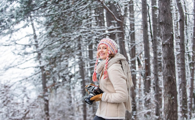 Vacanza di viaggio invernale. elegante viaggiatore hipster. donna che tiene la macchina fotografica. scattare una foto nella foresta invernale. Fotografo che fotografa il giorno di inverno nevoso. donna felice vestiti caldi moda.