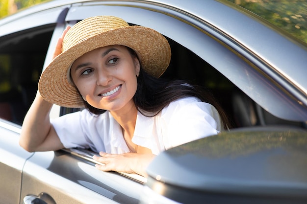 Vacanza di viaggio Una giovane bella donna con un cappello si siede in una macchina e sorride guardando in lontananza Stile di vita