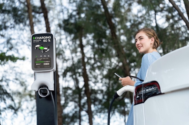 Vacanza in viaggio nella verde campagna con una bellissima giovane donna che ricarica il veicolo elettrico con energia alternativa Viaggio rispettoso dell'ambiente con un'auto elettrica Perpetua