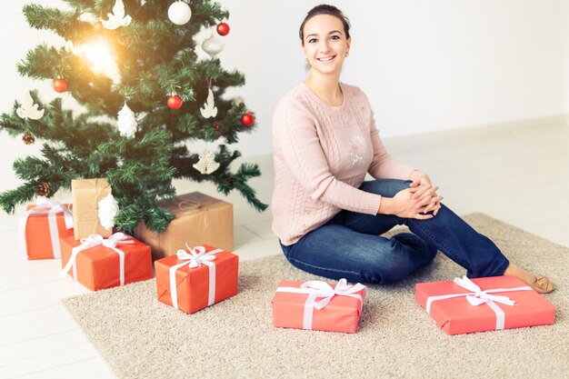 Vacanze, celebrazione e concetto festivo - Bella giovane donna seduta sotto l'albero di Natale