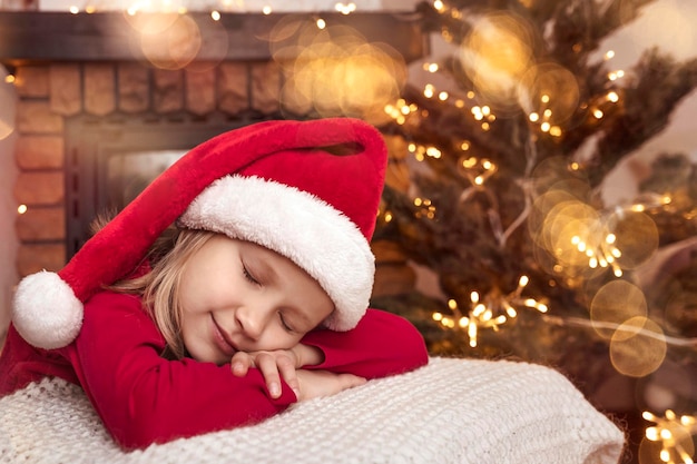 Vacanze di Natale e Capodanno in arrivo. Christmas Kid Girl in Santa Hat dorme aspettando Babbo Natale