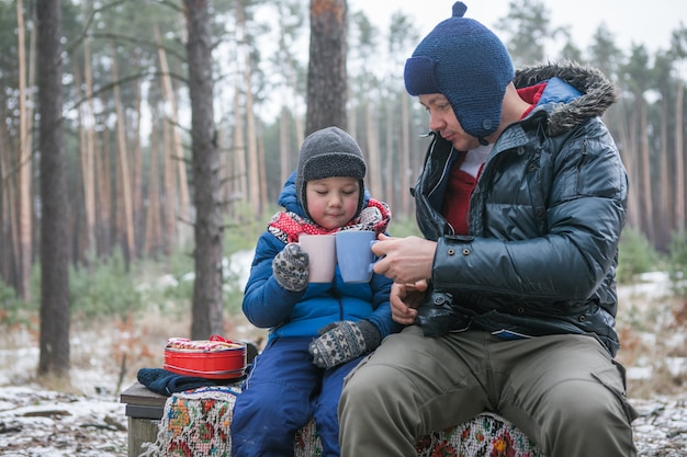 Vacanze di Natale, padre e figlio che bevono bevande calde di Capodanno. Famiglia felice in una passeggiata all'aperto nella soleggiata foresta invernale