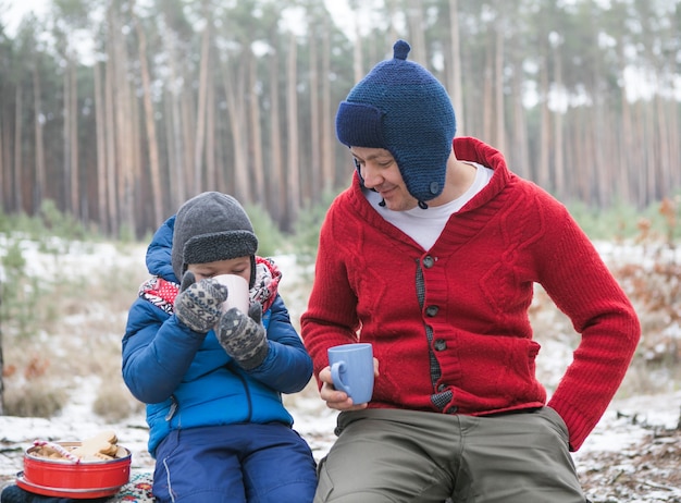 Vacanze di Natale, padre e figlio che bevono bevande calde di Capodanno. Famiglia felice in una passeggiata all'aperto nella soleggiata foresta invernale