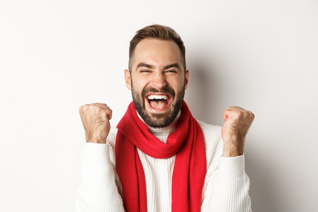 Vacanze di Natale. Primo piano del vincitore del ragazzo felice, celebrando la vittoria, alzando le mani e gridando sì di gioia, raggiungere l'obiettivo, sfondo bianco