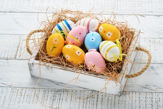 Vacanze di Pasqua Uova di Pasqua colorate nel cesto di legno su sfondo di legno bianco Biglietto di auguri di Pasqua Spazio per la copia della vista dall'alto