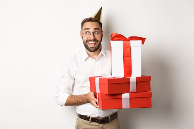 Vacanze e celebrazione. Uomo eccitato che fa festa di compleanno e riceve regali, sembra felice, in piedi su sfondo bianco