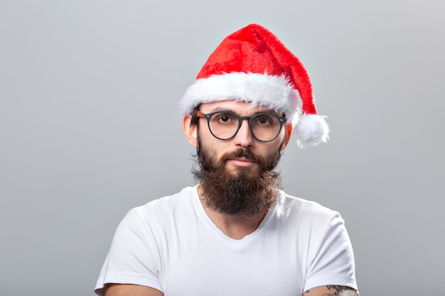 Vacanze e concetto di persone - Ritratto di un bell'uomo brutale con il cappello di Natale Su sfondo grigio.