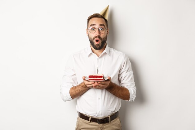 Vacanze e festeggiamenti uomo felice che fa festa di compleanno esprimendo desideri sulla torta di compleanno e sorridendo in piedi...