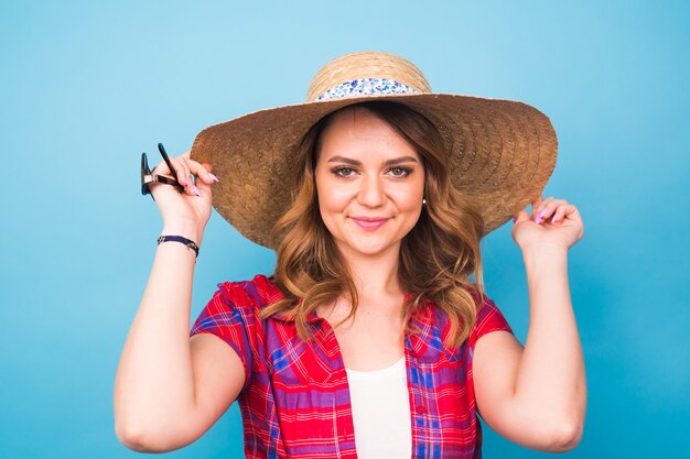 Vacanze, estate, moda e concetto di persone - Ragazza in cappello di paglia di vestiti alla moda. Ritratto di donna affascinante su sfondo blu con copia spazio vuoto.