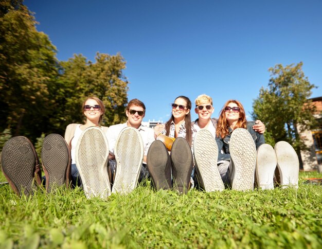 vacanze estive, amicizia, tempo libero e concetto di persone - primo piano di studenti o adolescenti seduti sull'erba e in giro al campus o al parco