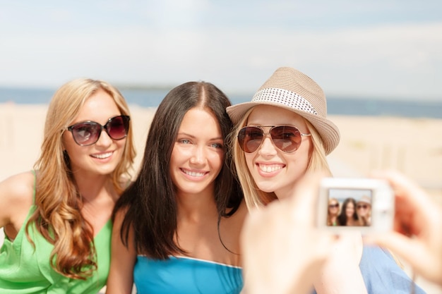 vacanze estive e concetto di vacanza - ragazze sorridenti che scattano foto con la fotocamera digitale al bar sulla spiaggia