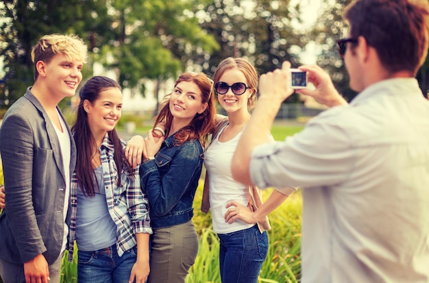 vacanze estive, elettronica e concetto adolescenziale - gruppo di adolescenti sorridenti che scattano foto con la fotocamera digitale all'esterno