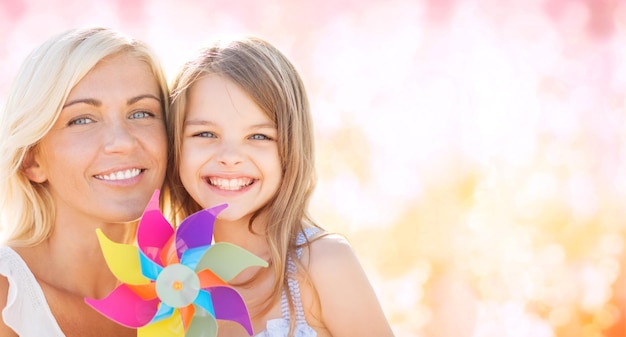 vacanze estive, famiglia, bambini e concetto di persone - madre e ragazza felici con il giocattolo della girandola su sfondo di luci rosa