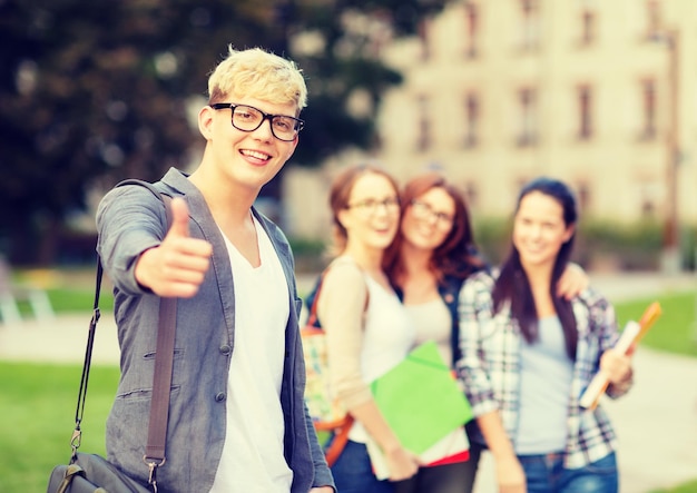 vacanze estive, istruzione, campus e concetto adolescenziale - studente maschio sorridente in occhiali neri con gruppo nella parte posteriore che mostra i pollici in su