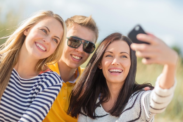 vacanze estive, vacanze, concetto di persone felici - gruppo di amici che prendono selfie con il cellulare sulla spiaggia