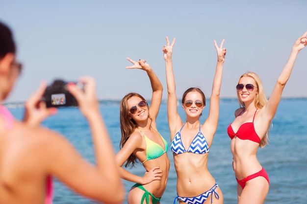 vacanze estive, vacanze, gesto e concetto di persone - gruppo di donne sorridenti che fotografano con la fotocamera e mostrano un sospiro di pace sulla spiaggia