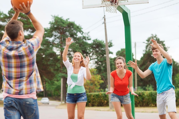 vacanze estive, vacanze, giochi e concetto di amicizia - gruppo di adolescenti sorridenti che giocano a basket all'aperto