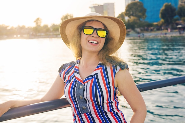 Vacanze estive, vacanze, viaggi e concetto di persone - sorridente giovane donna che indossa occhiali da sole e cappello sulla spiaggia sopra il mare.