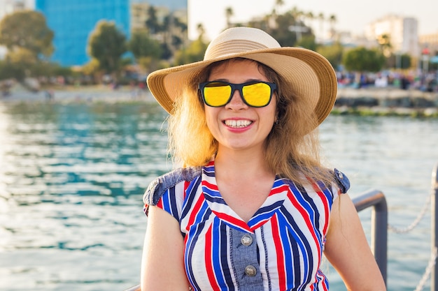 Vacanze estive, vacanze, viaggi e concetto di persone - sorridente giovane donna che indossa occhiali da sole e cappello sulla spiaggia sullo sfondo del mare.