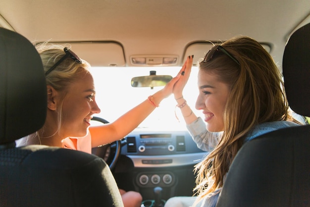 vacanze estive, vacanze, viaggi, viaggio su strada e concetto di persone - ragazze adolescenti felici o giovani donne che guidano in auto e fanno un gesto di cinque