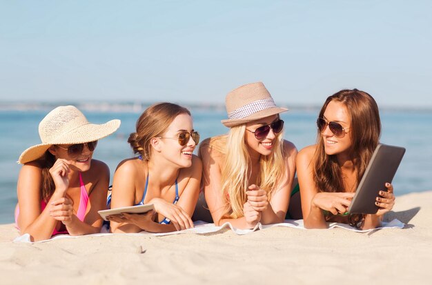 vacanze estive, viaggi, tecnologia e concetto di persone - gruppo di donne sorridenti in occhiali da sole con computer tablet pc sdraiati sulla spiaggia